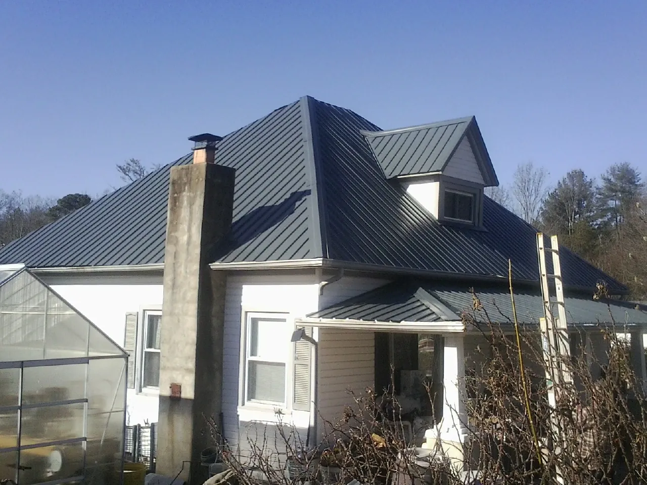 Dark blue standing seam metal roof on a white farmhouse with dormer — Slate & Tile Roof Repair by Roofing Brothers in Silver Gate