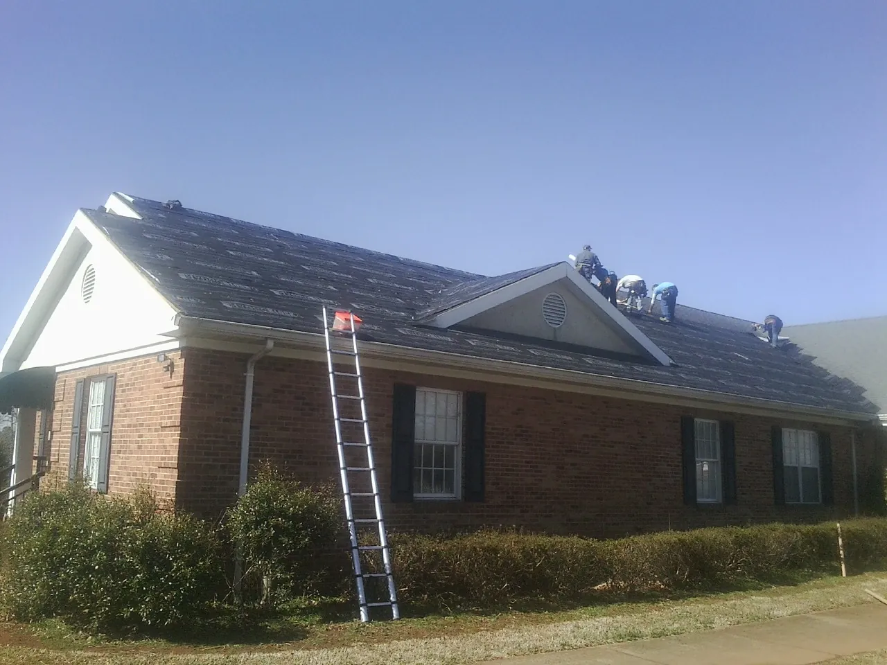 Crew tearing shingles off a brick ranch roof with a ladder set — Metal Roof Repair work by our crew in Silver Gate