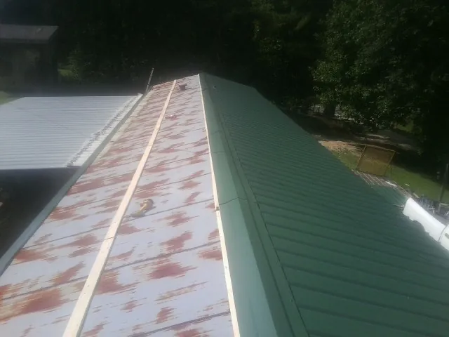 Old rusted panels beside newly installed green metal roofing — Wind Damage Roof Repair by Roofing Brothers in Silver Gate