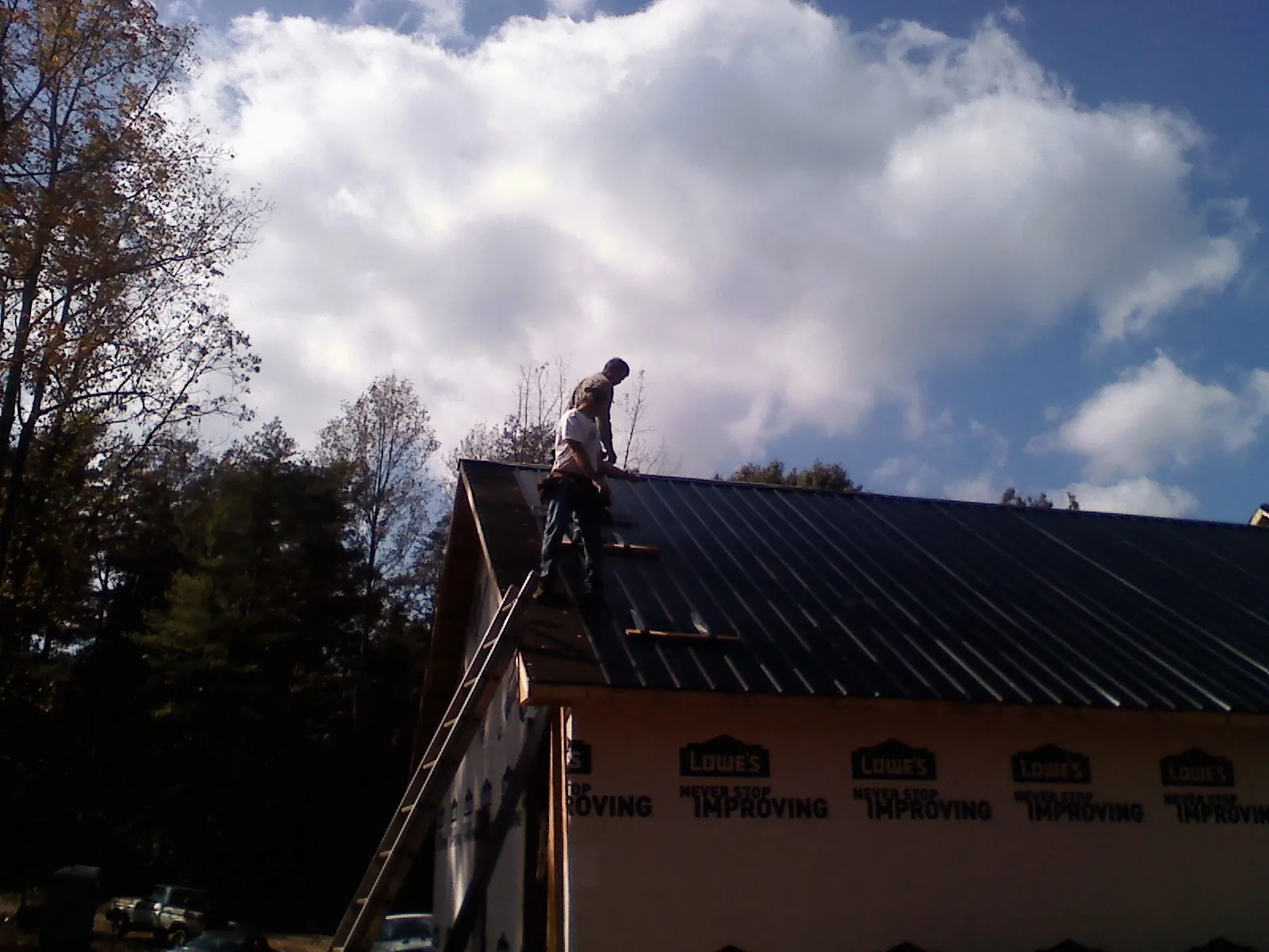 Roofer fastening dark metal panels high against a cloudy sky, from a Roof Inspection job in Silver Gate